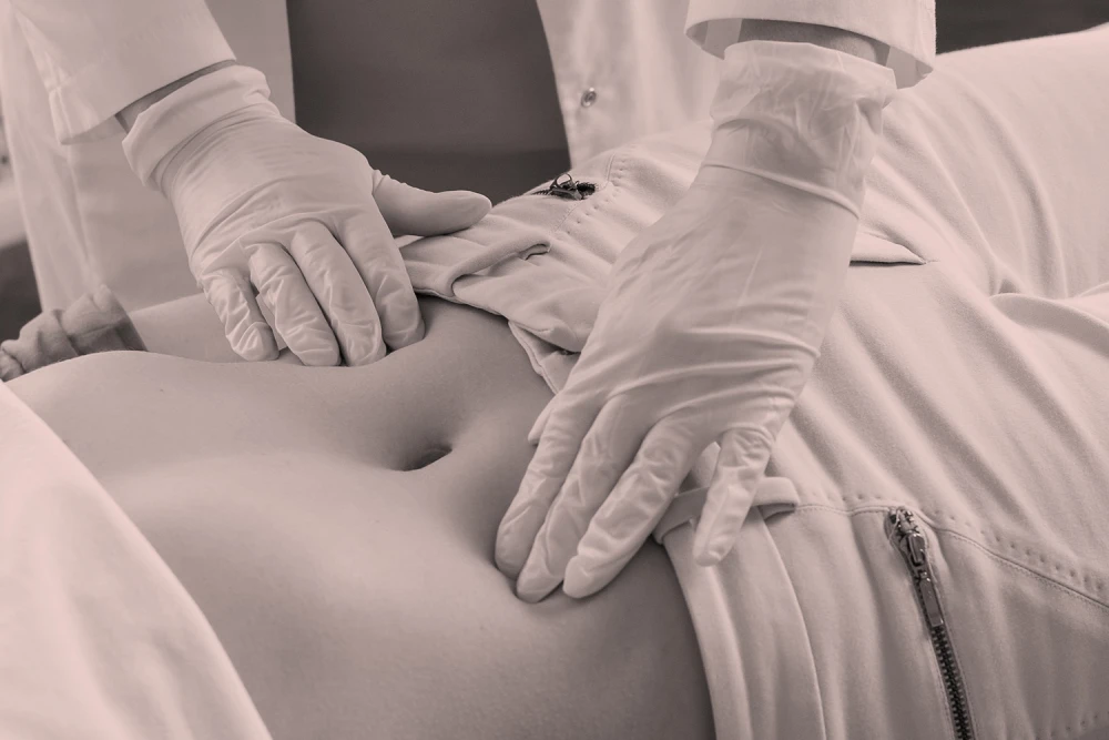 Doctor wearing gloves palpating patient's abdomen during a medical check-up to assess internal pain or digestive issues.