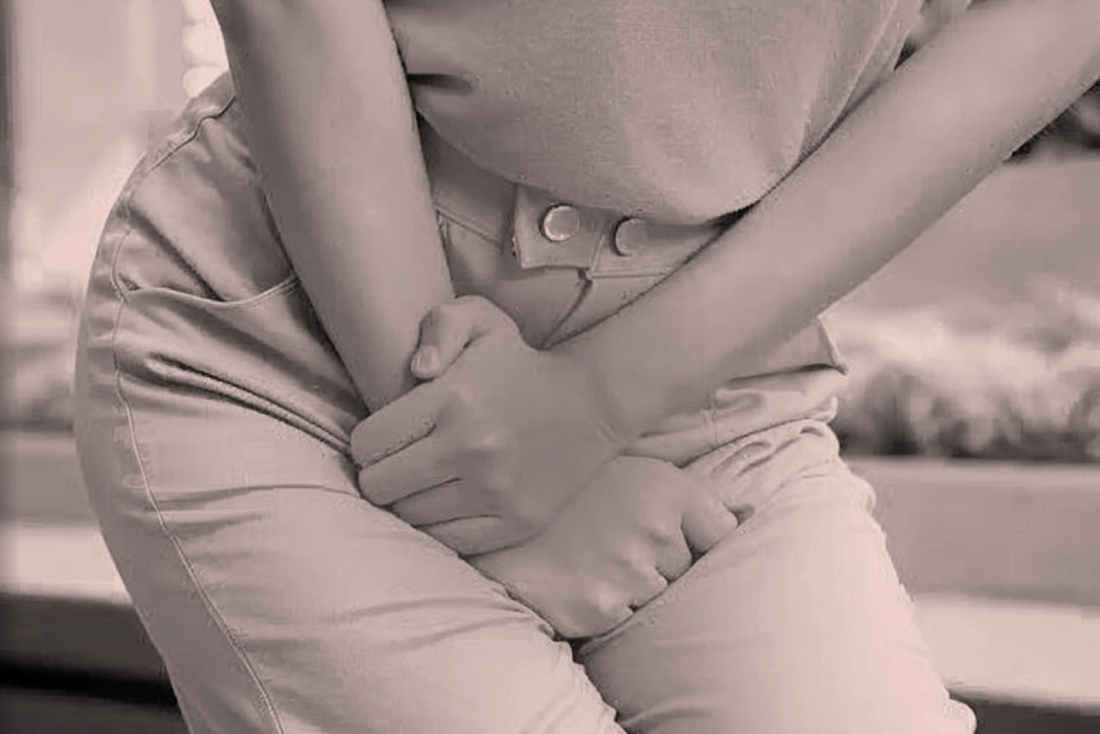 A woman clenching her lower abdomen and legs, suggesting urgency or discomfort from a urinary tract or bladder condition.
